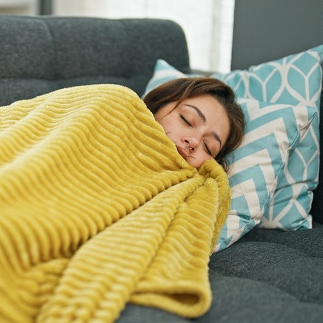 Nainen makaa sohvalla keltainen peitto päällään.
