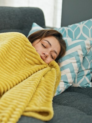 Nainen makaa sohvalla keltainen peitto päällään.